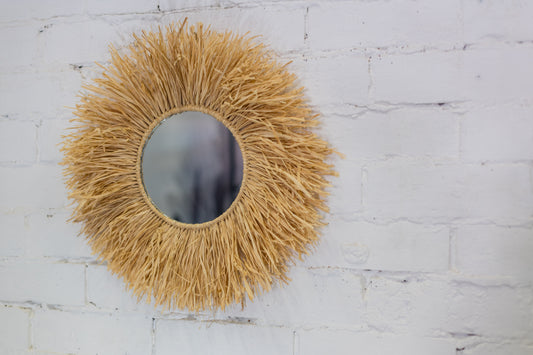Round mirror with a natural straw-like frame on a white brick wall.