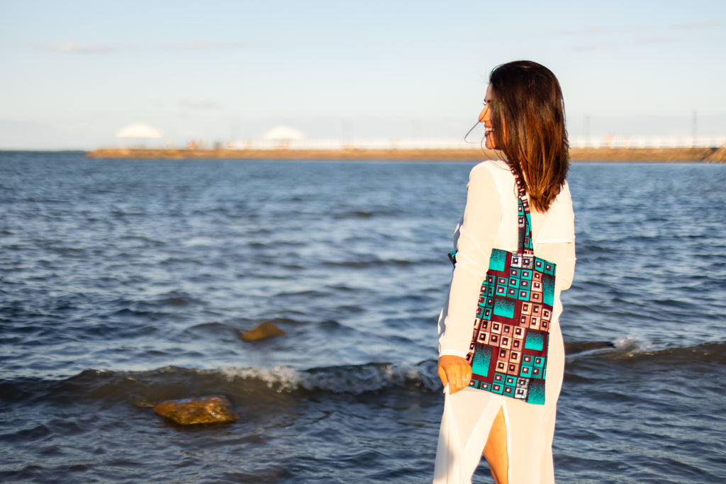 Woman standing by a body of water wearing a colorful tote bag.
