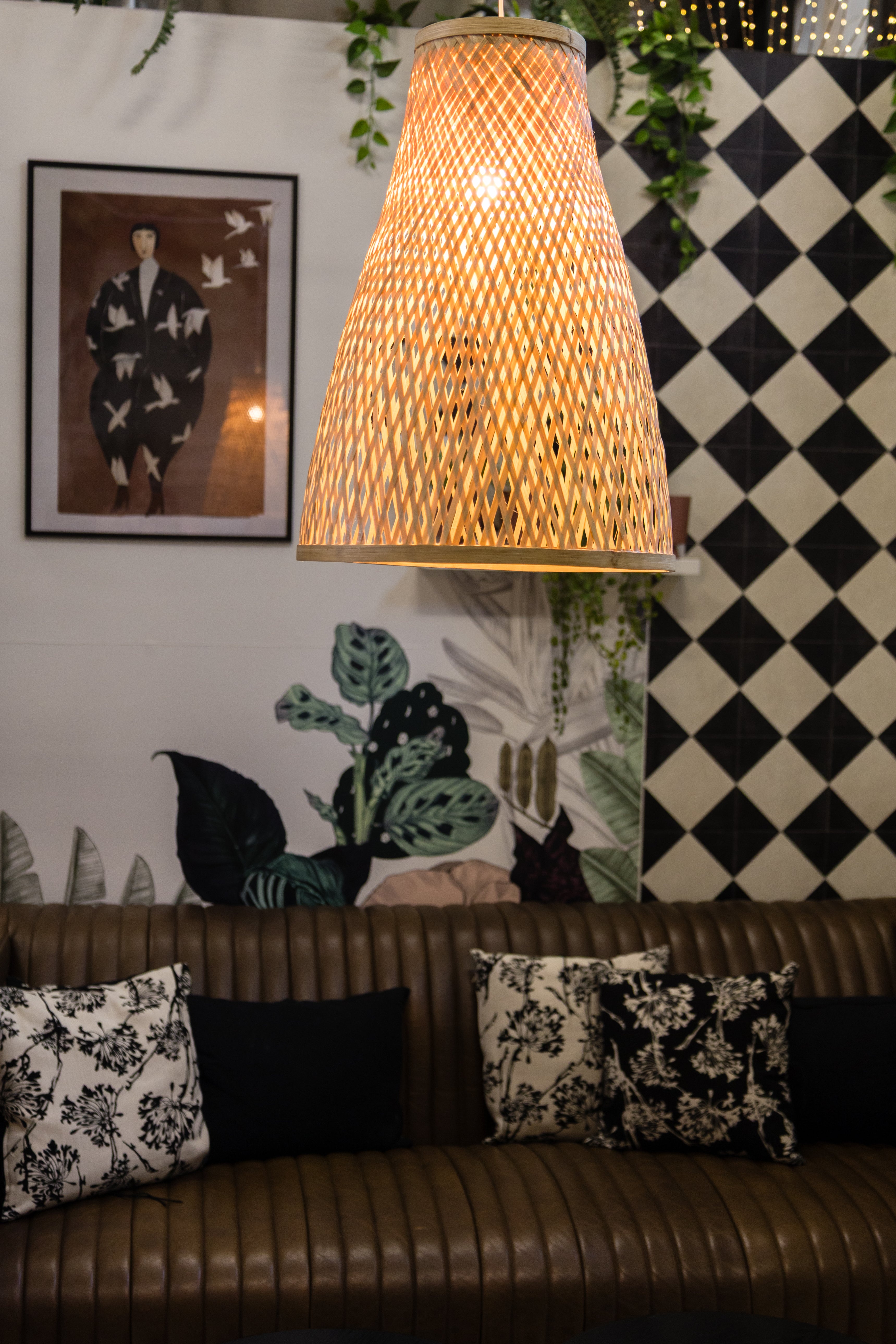 Woven lampshade hanging above a sofa with decorative pillows against a checkered wall.