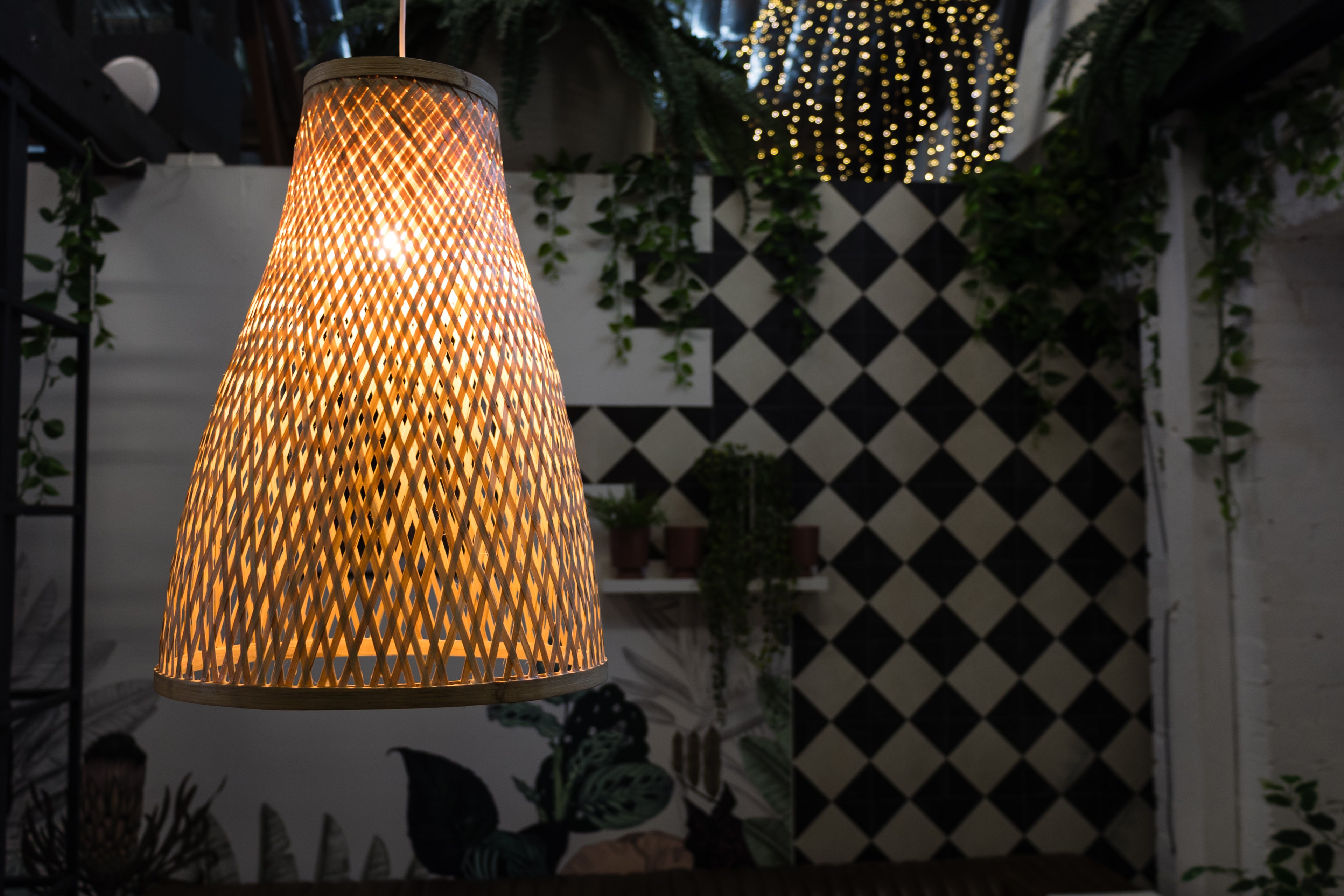 Woven lampshade hanging in a room with a checkered wall and plants.