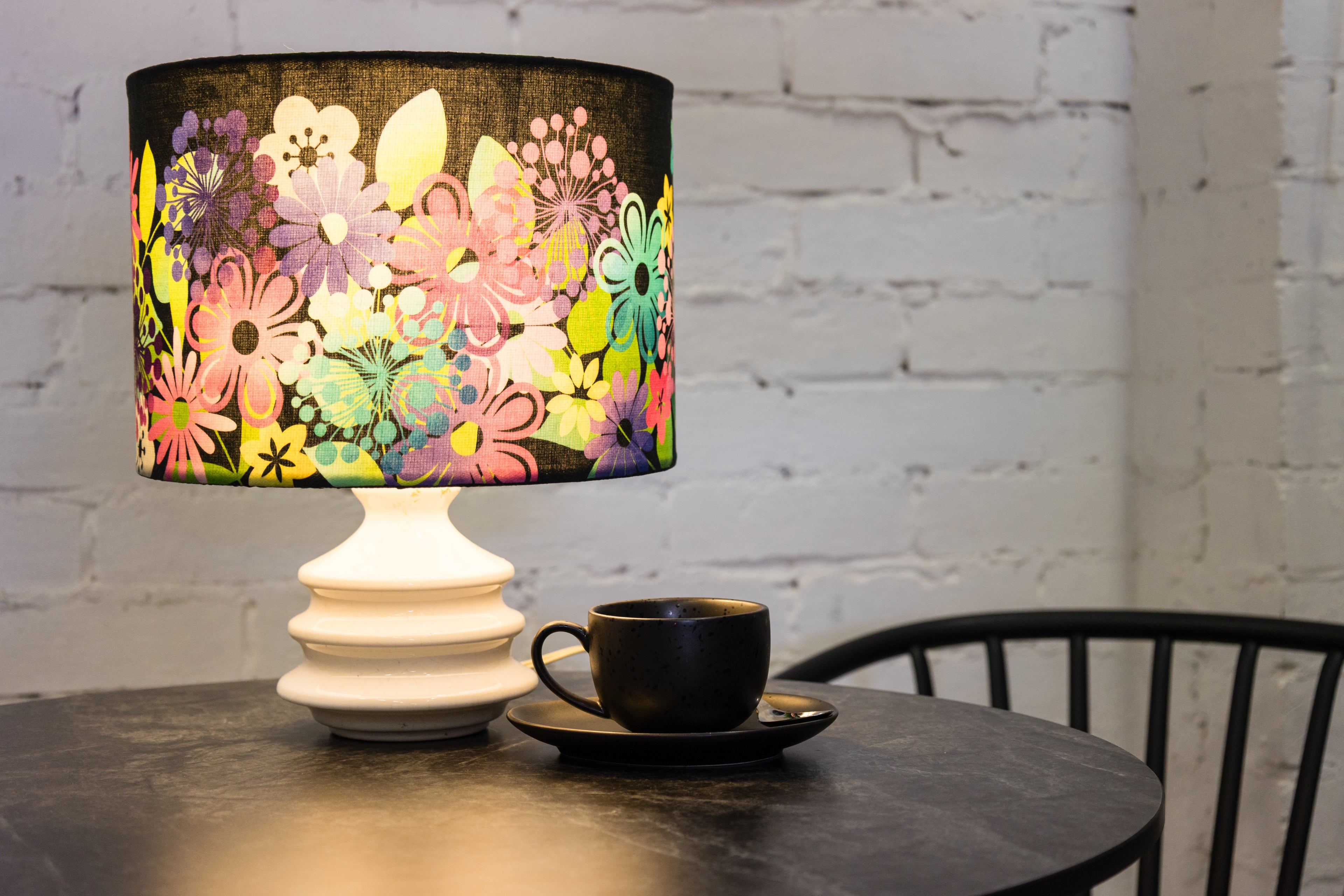 Decorative lamp with colourful floral shade on a table with a cup and saucer.