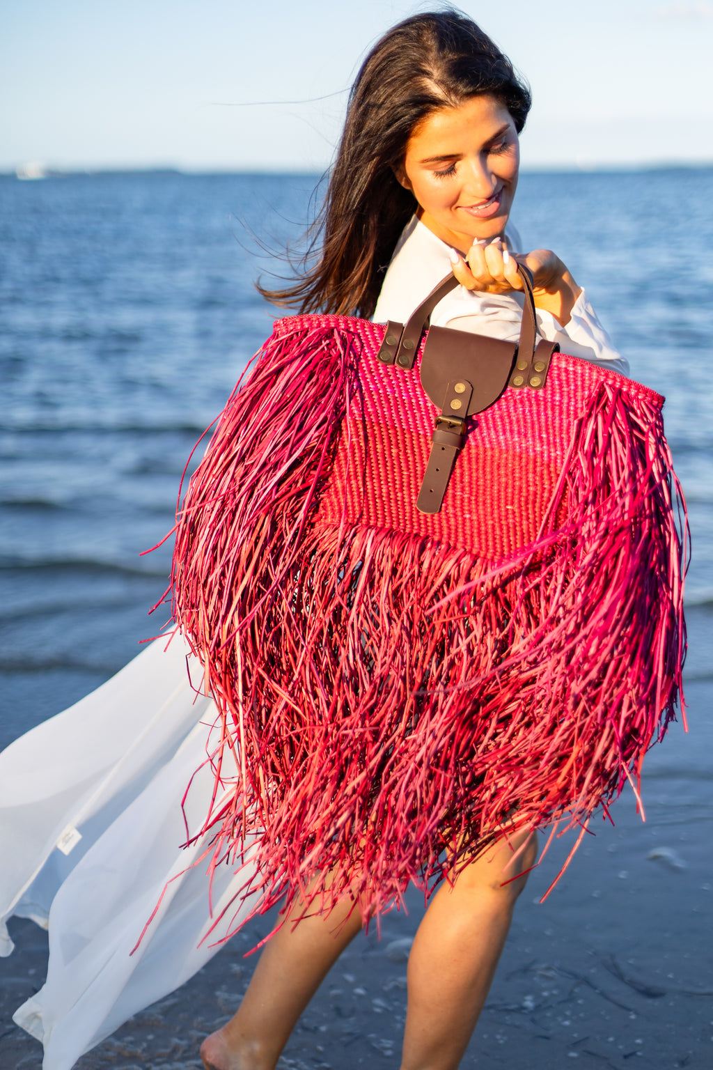 Woman holding a pink and red fringed bag on a beach