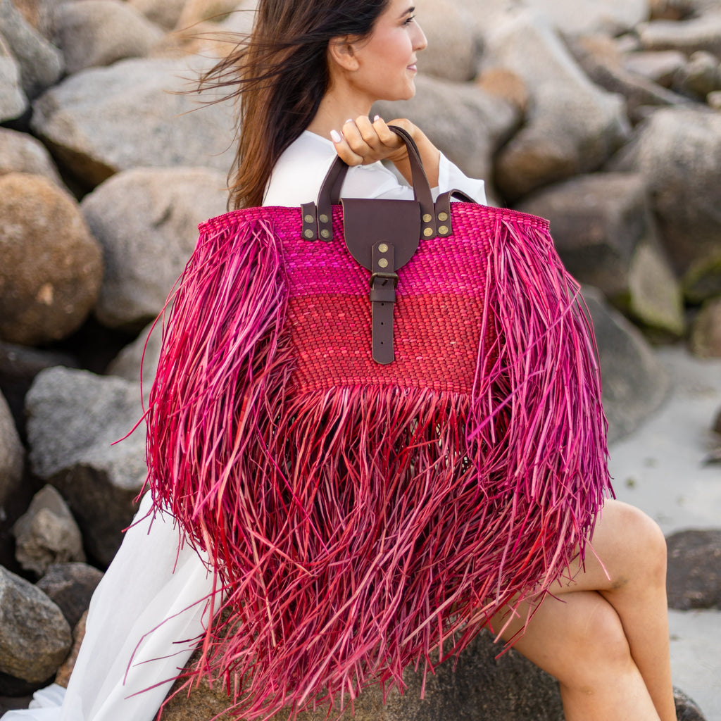 Woman holding a pink and red fringed handbag on a rocky beach