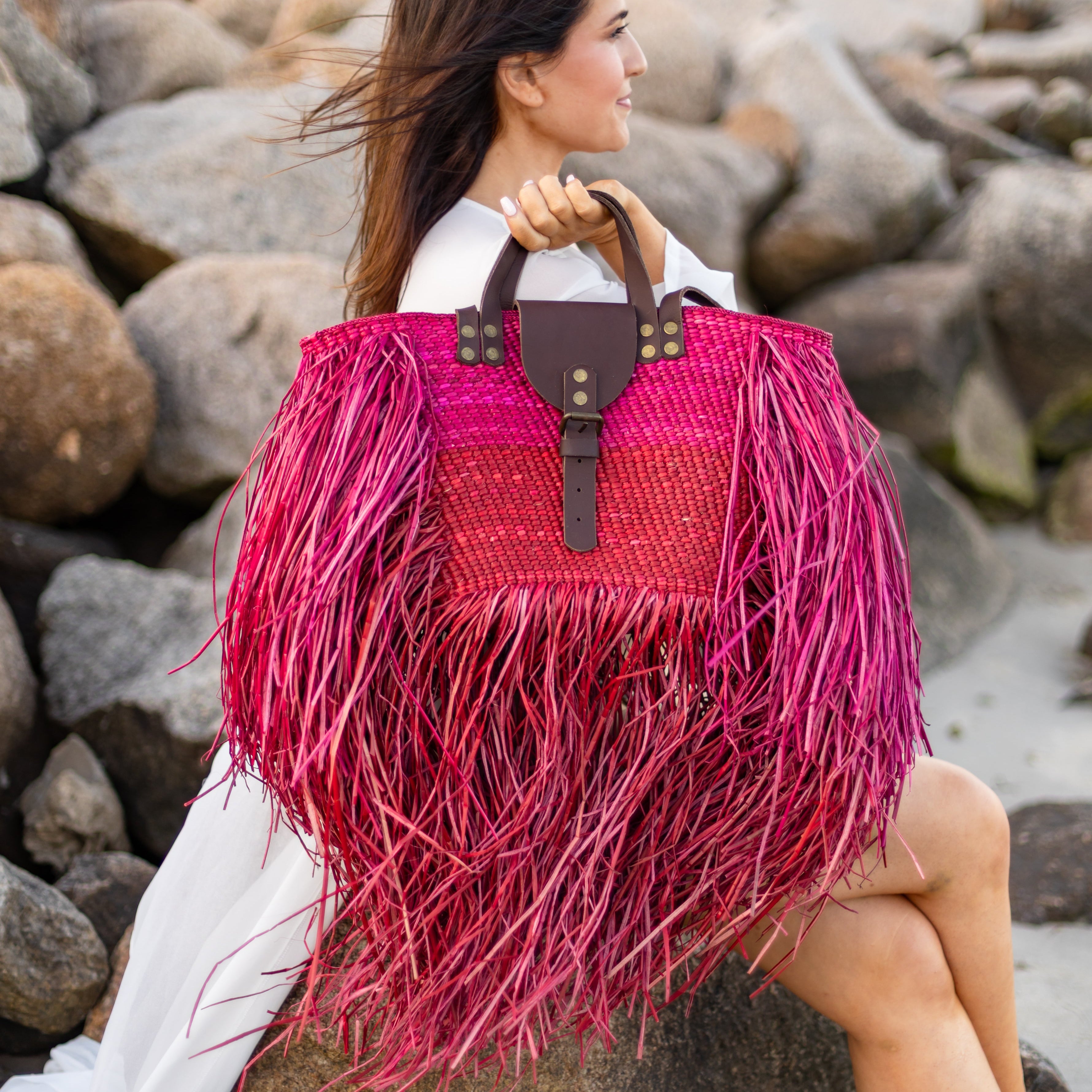 Woman holding a pink and red fringed handbag on a rocky beach