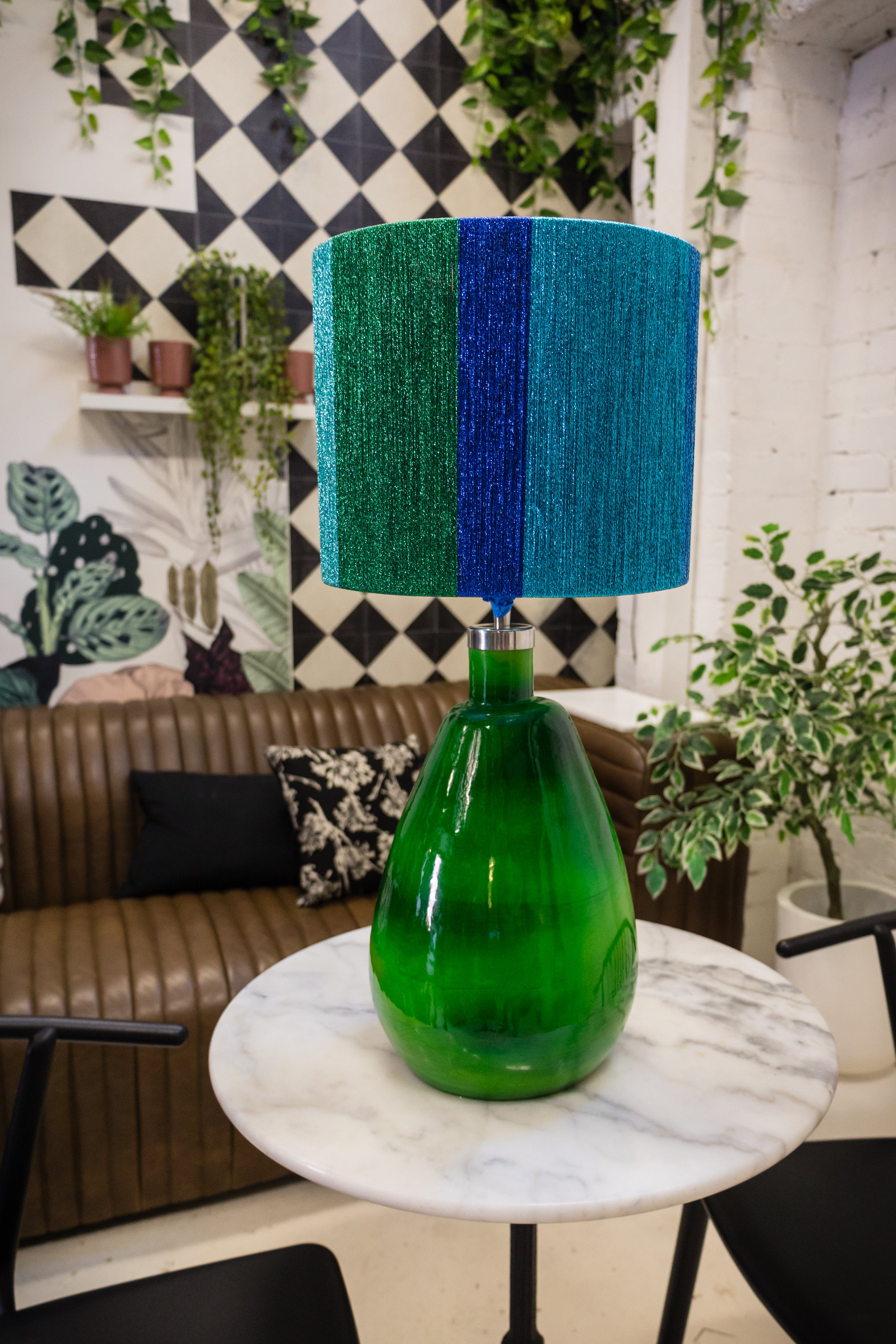 Green glass lamp with blue striped shade on a marble table in a stylish room.