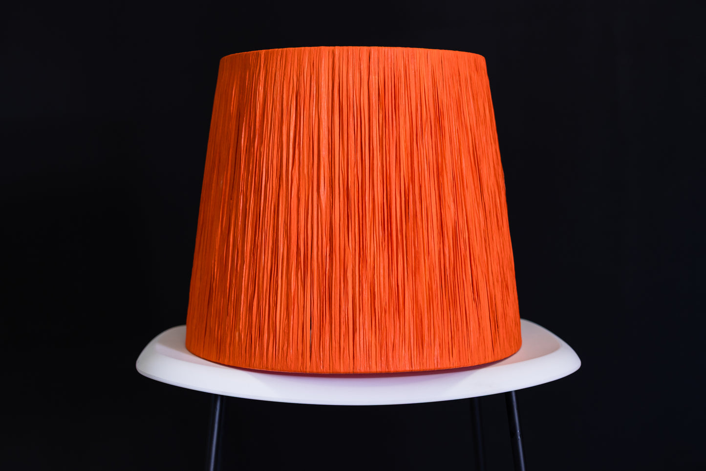 Orange wrapped lampshade on a white base against a black background