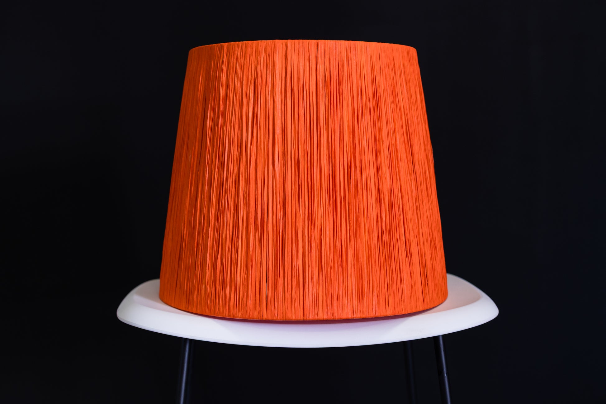 Orange wrapped lampshade on a white base against a black background