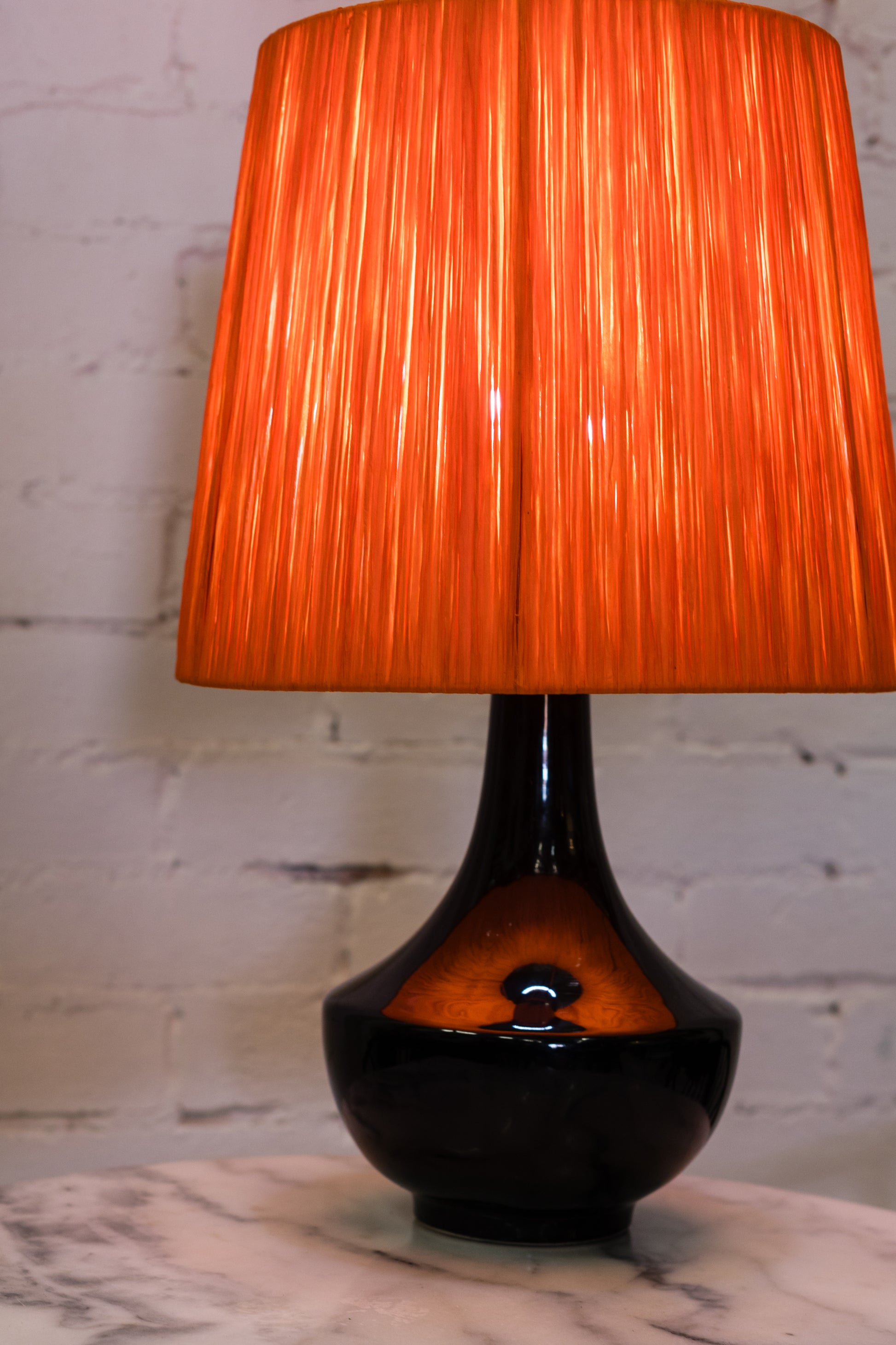Table lamp with an orange raffia wrapped shade and black base on a marble surface.