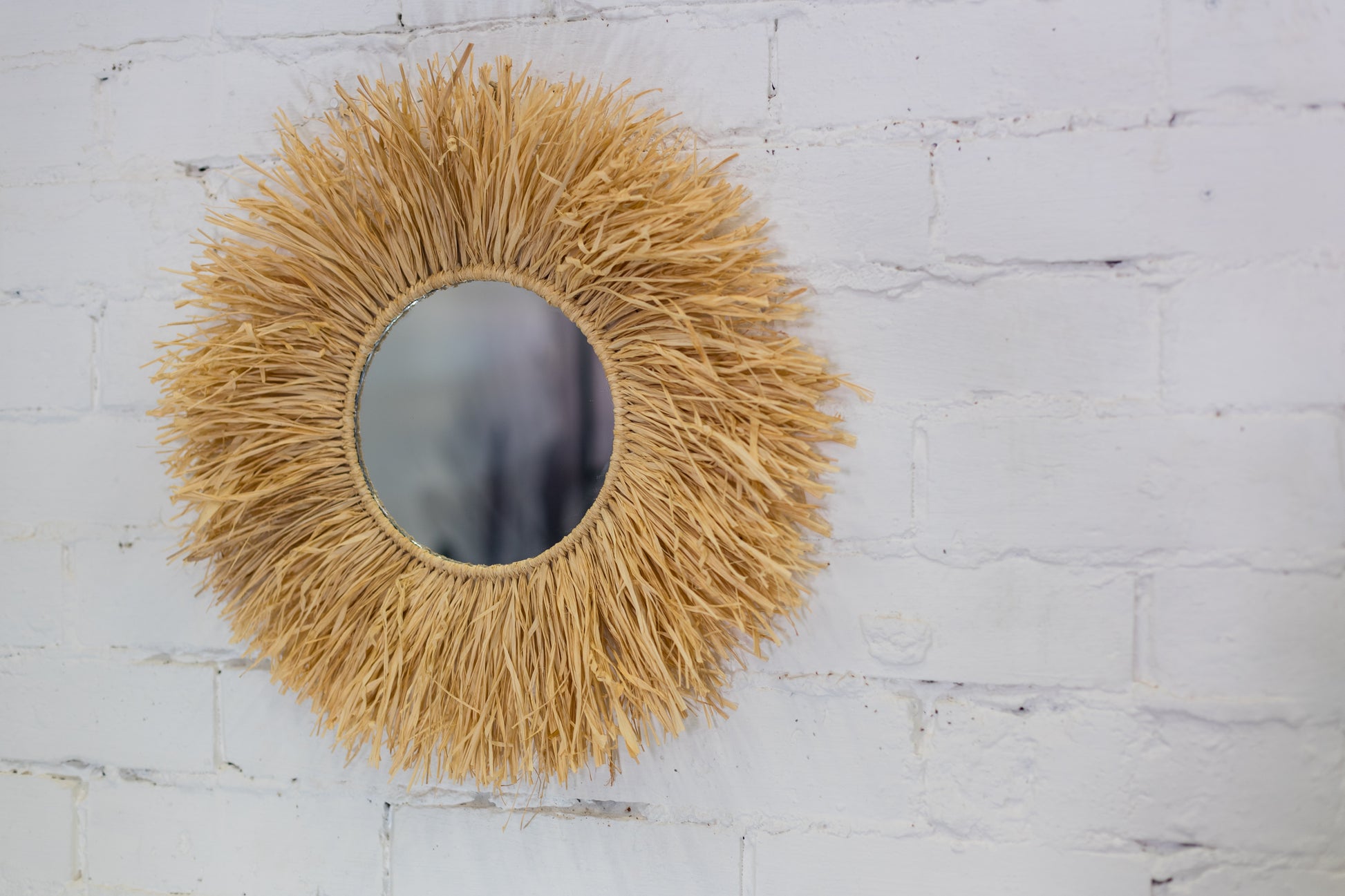 Round mirror with a natural straw-like frame on a white brick wall.