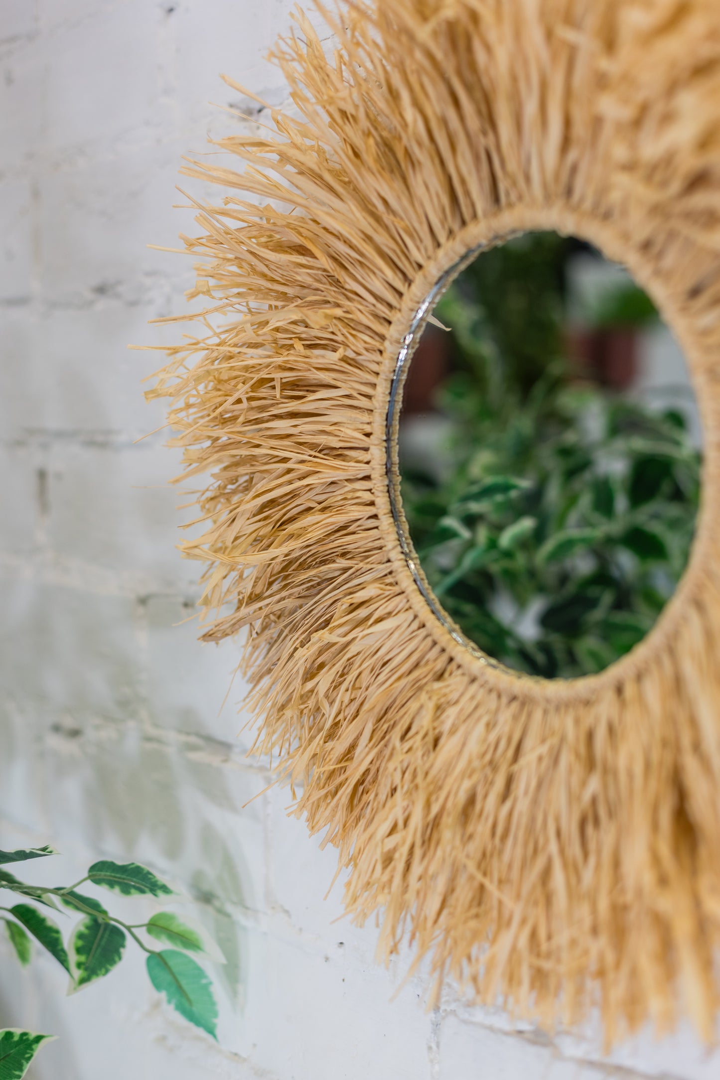 Round mirror with raffia frame on a light wooden surface