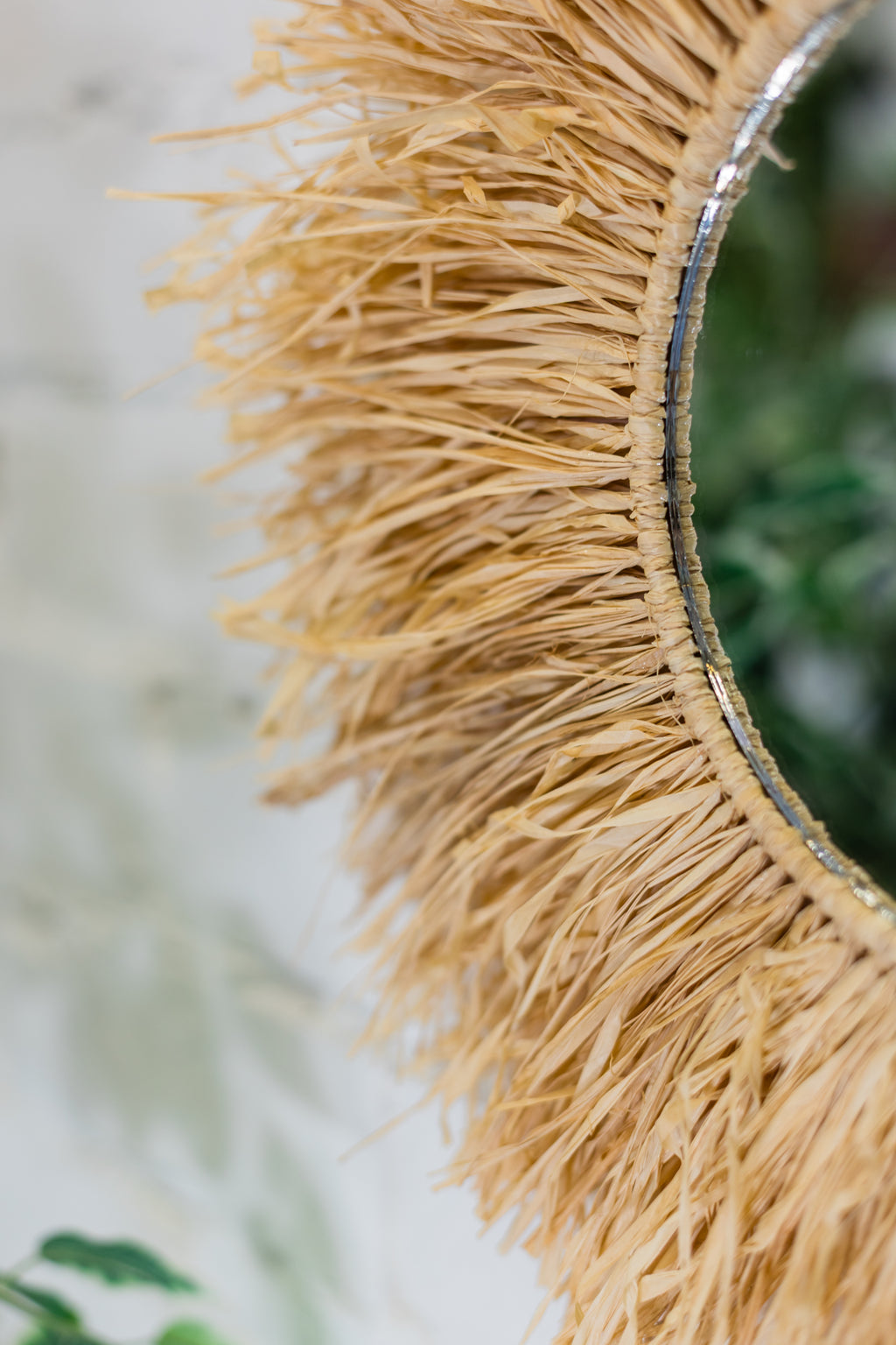 Close-up of a decorative mirror with raffia fringe trim.