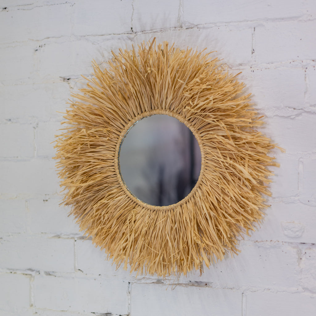 Round mirror with a natural, straw-like frame on a white textured wall.