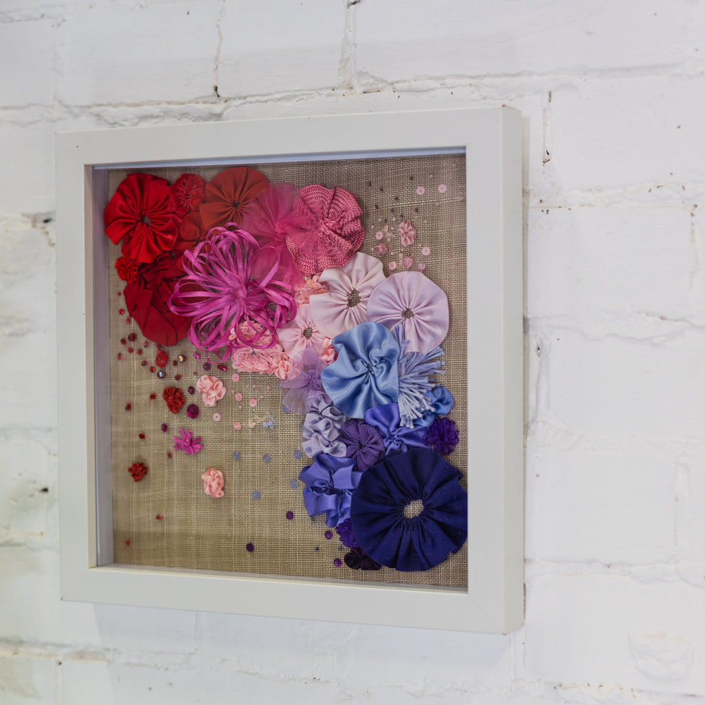 Framed artwork with colourful ribbon flowers on a white brick wall background