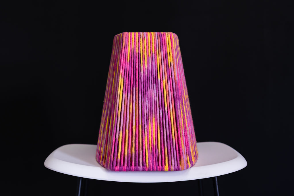 Colorful lampshade with pink and yellow stripes on a white base against a black background