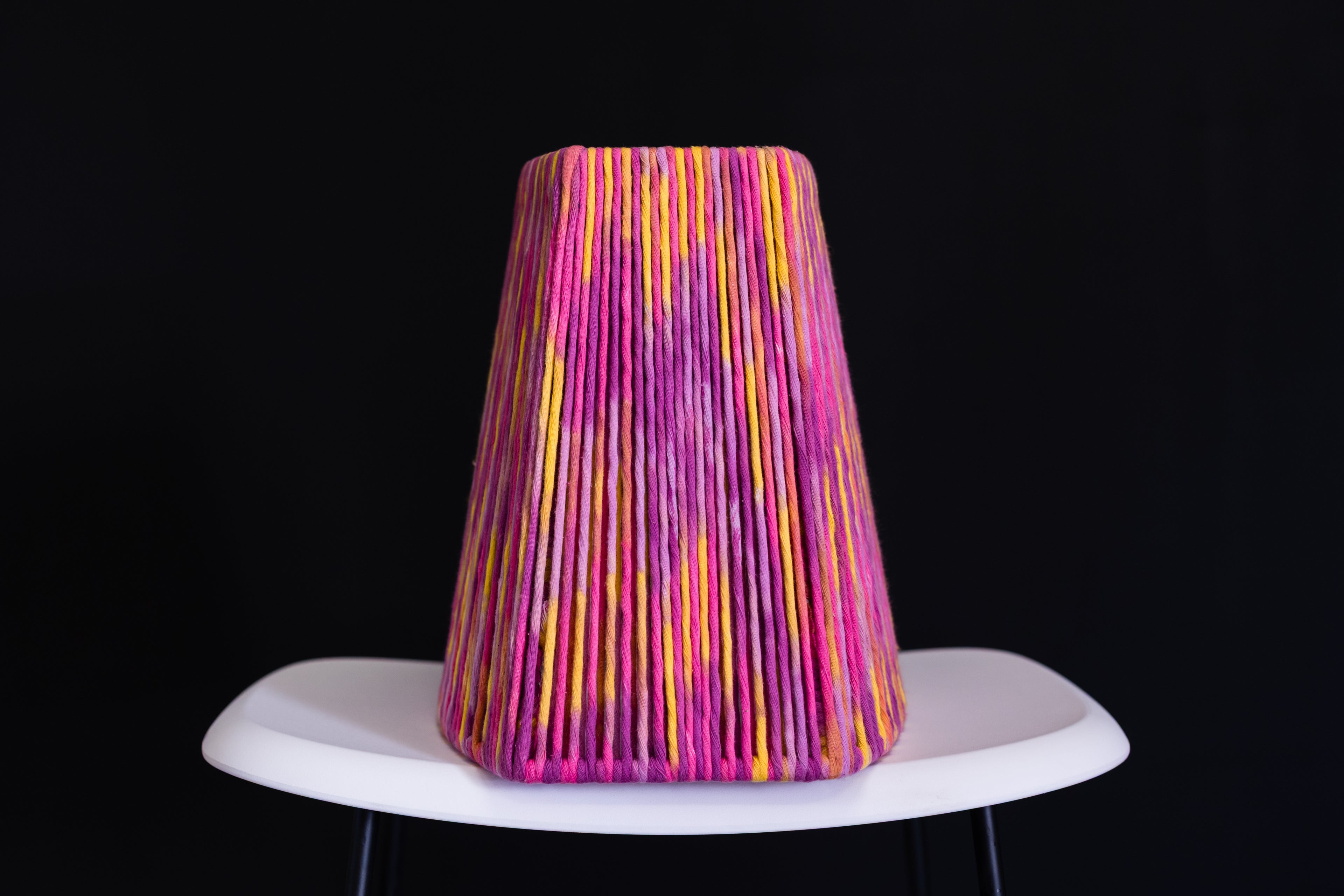 Colorful lampshade with pink and yellow stripes on a white base against a black background