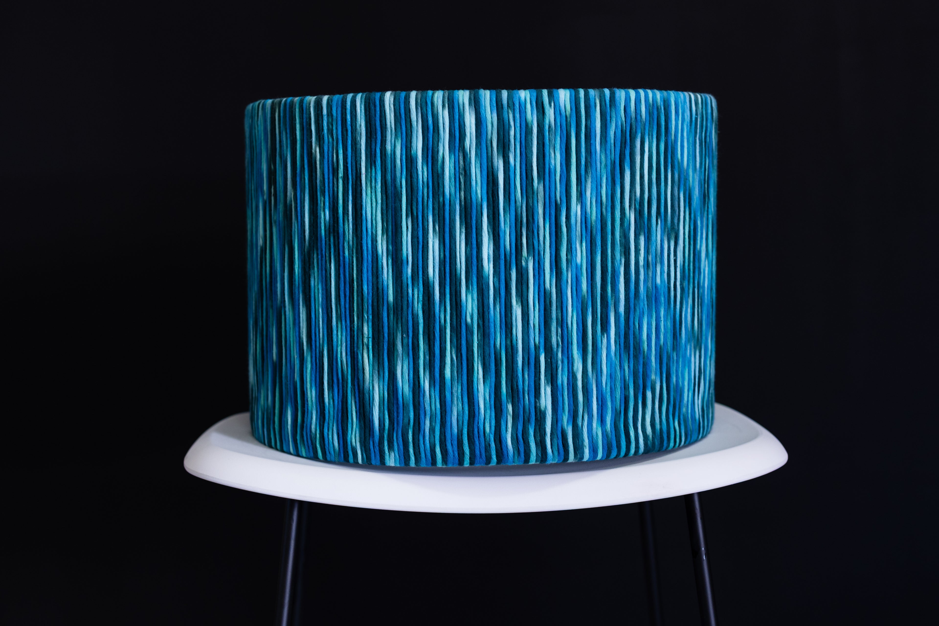 Blue textured cake on a white stand against a black background