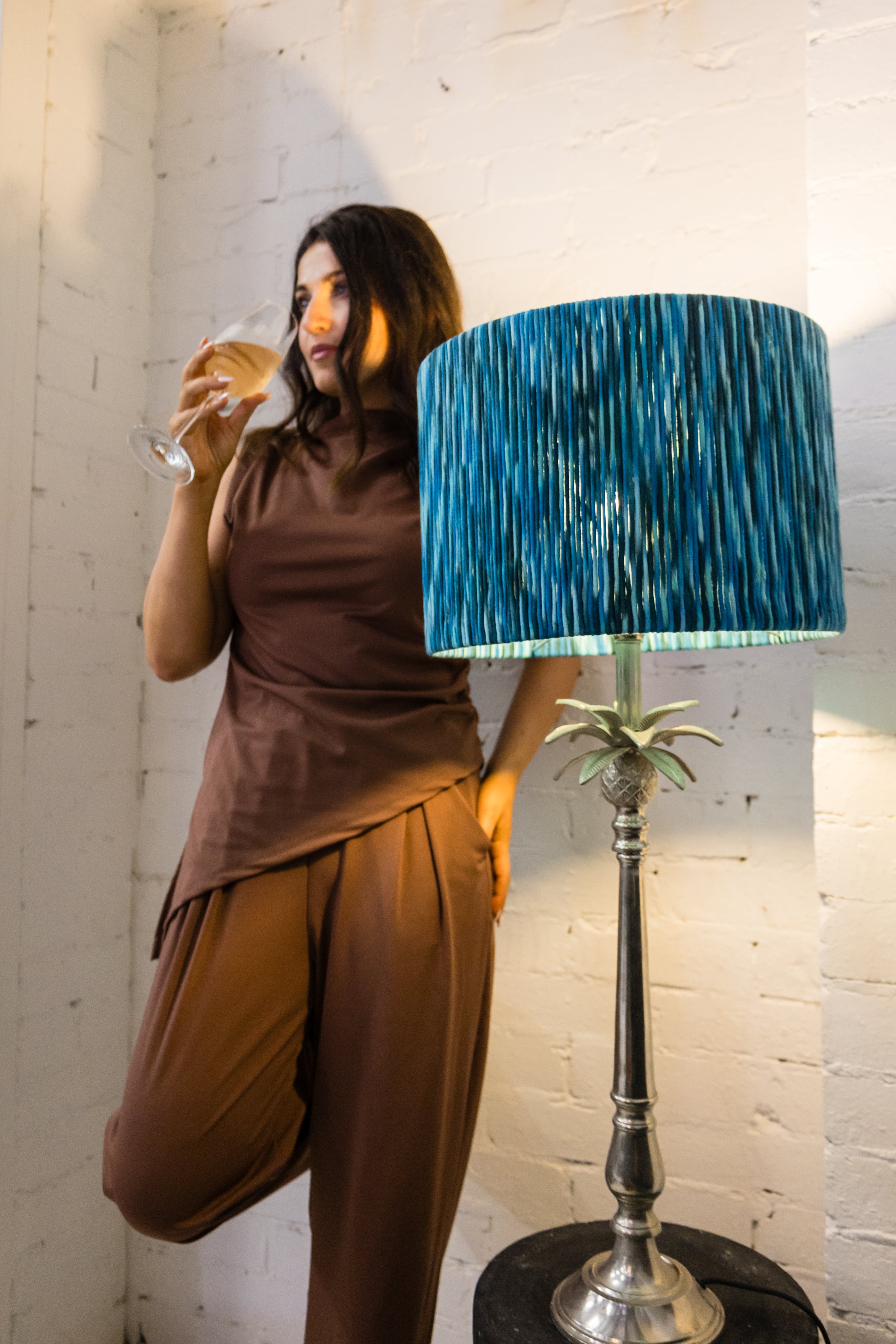 Woman holding a glass of wine standing next to a lamp with a blue shade.