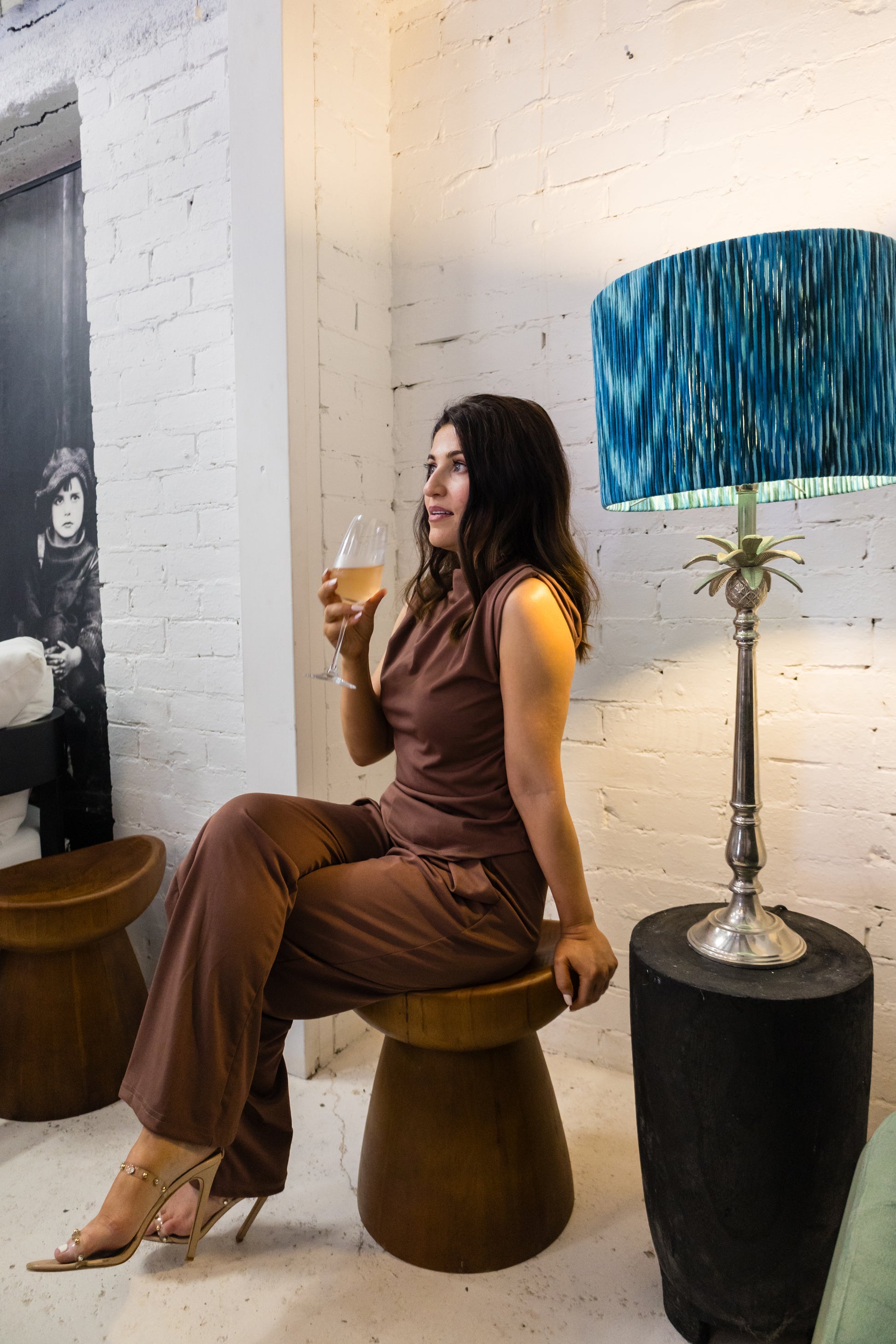 Woman sitting on a stool in a stylish room with a lamp and white walls.