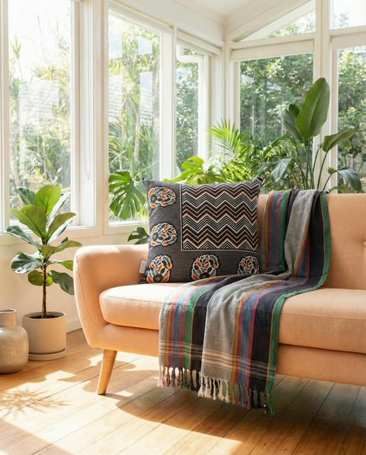 Orange sofa with a colorful throw rug and orange, black and white cushion in a sunlit room with large windows and plants.