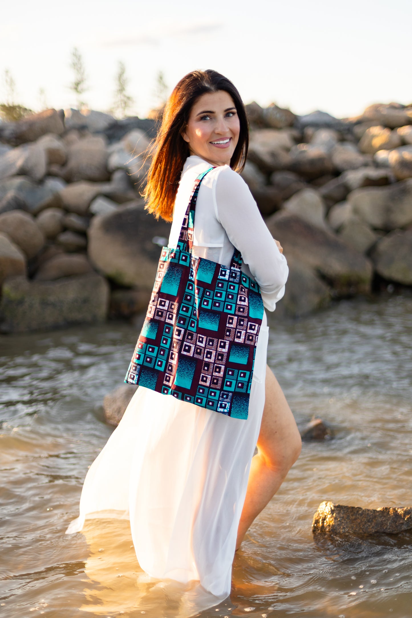 Woman standing in water wearing a colorful patterned dress with a white cardigan.