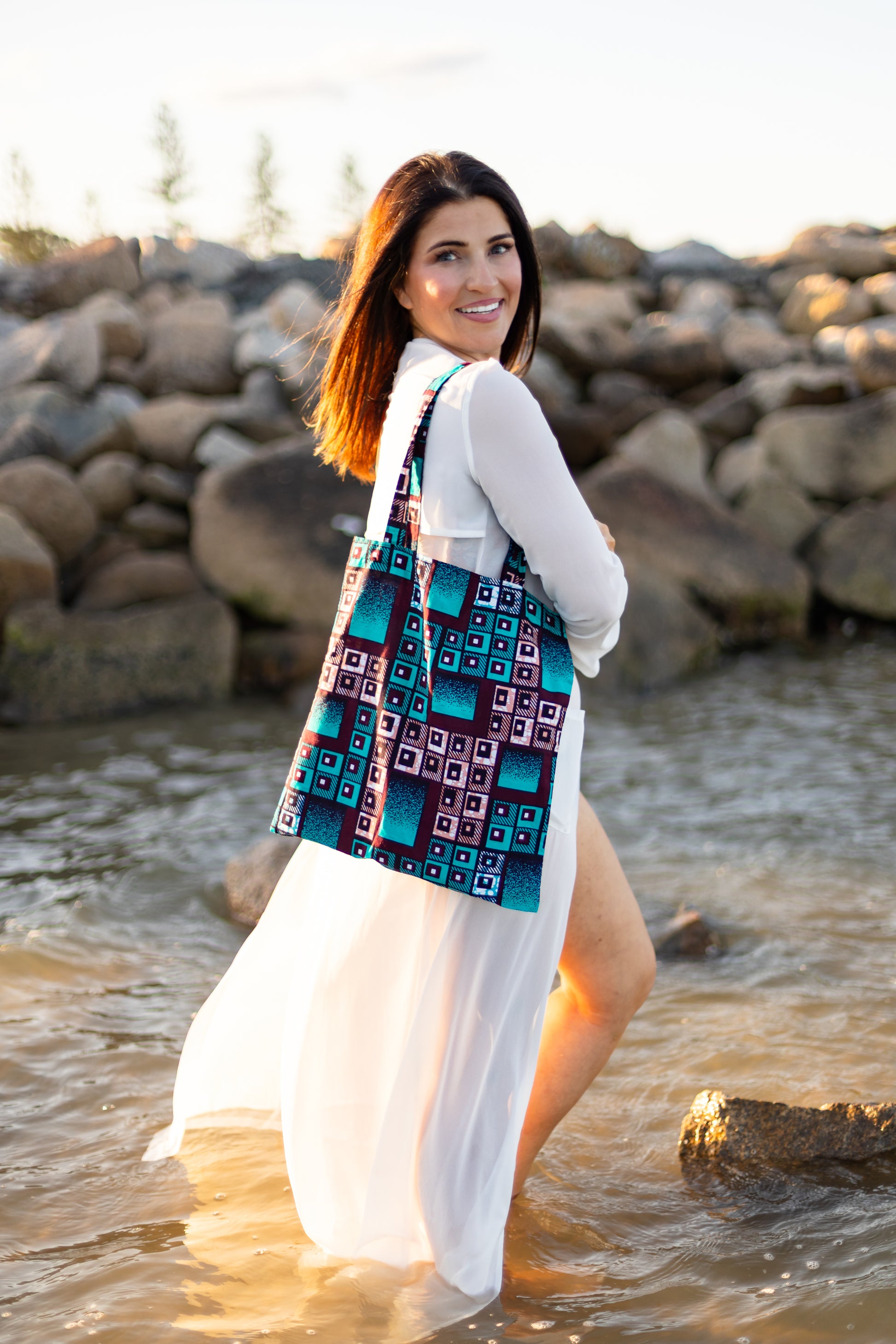 Woman standing in water wearing a colorful patterned dress with a white cardigan.