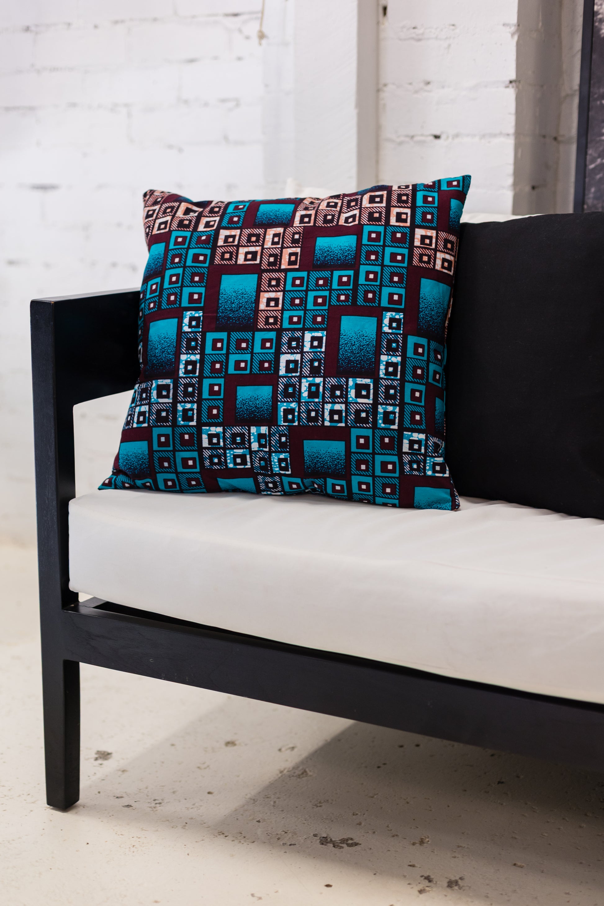 Decorative pillow with geometric pattern on a black couch against a white brick wall.
