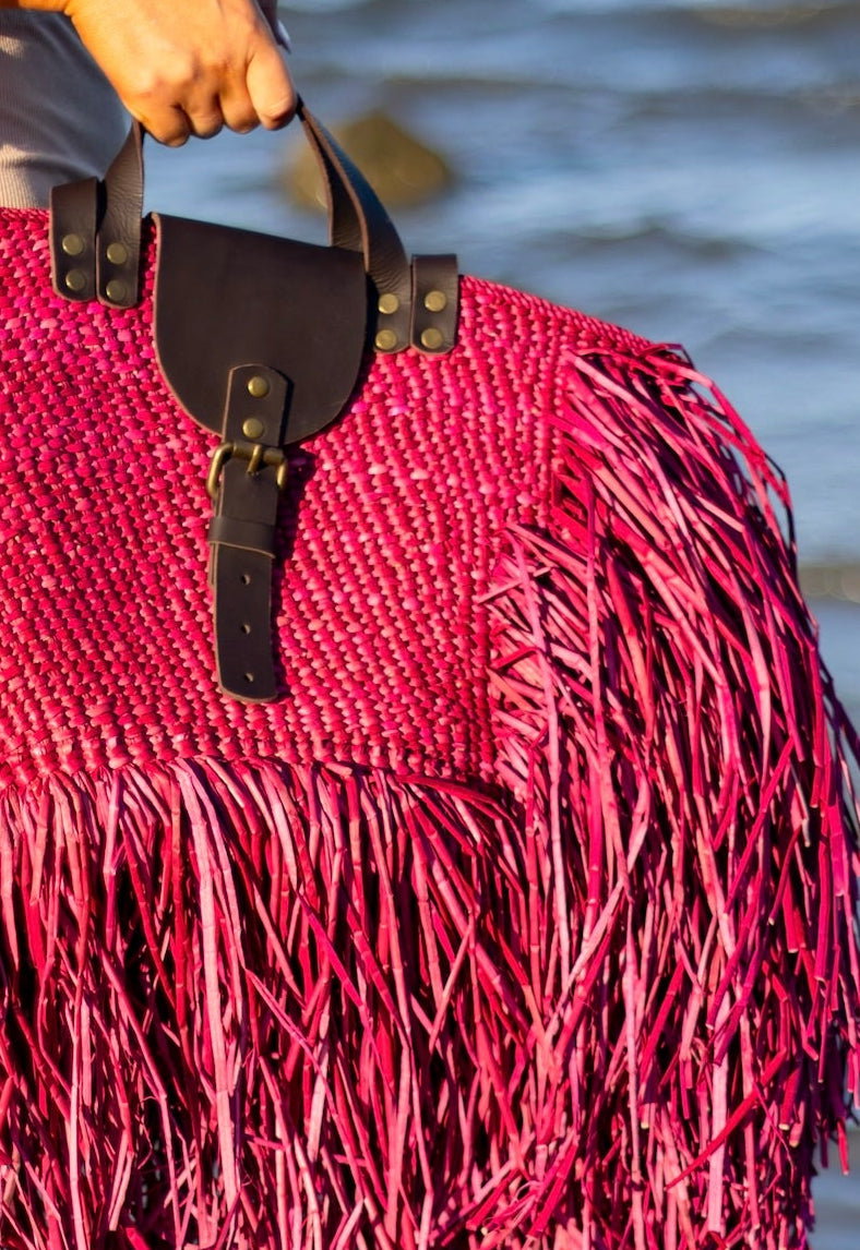 Person holding a red fringed bag by the water