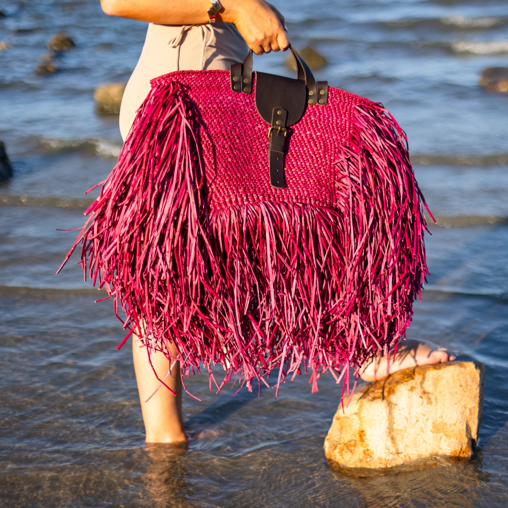 Person holding a red fringed handbag on a beach