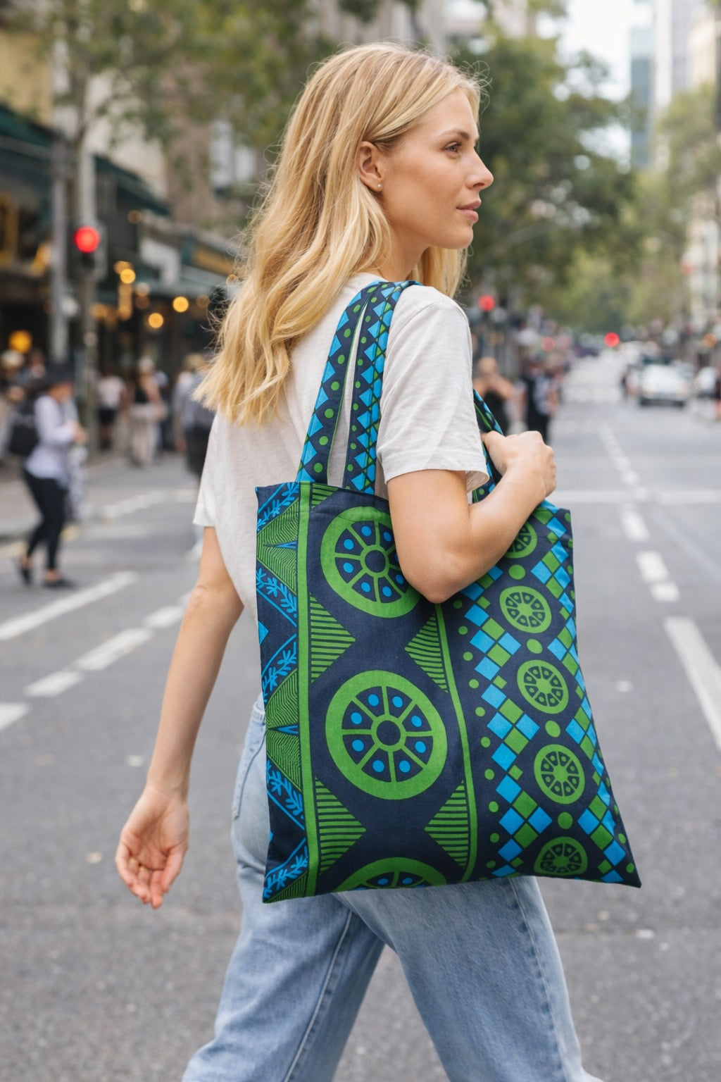 Woman walking on a city street holding a green and blue patterned bag.