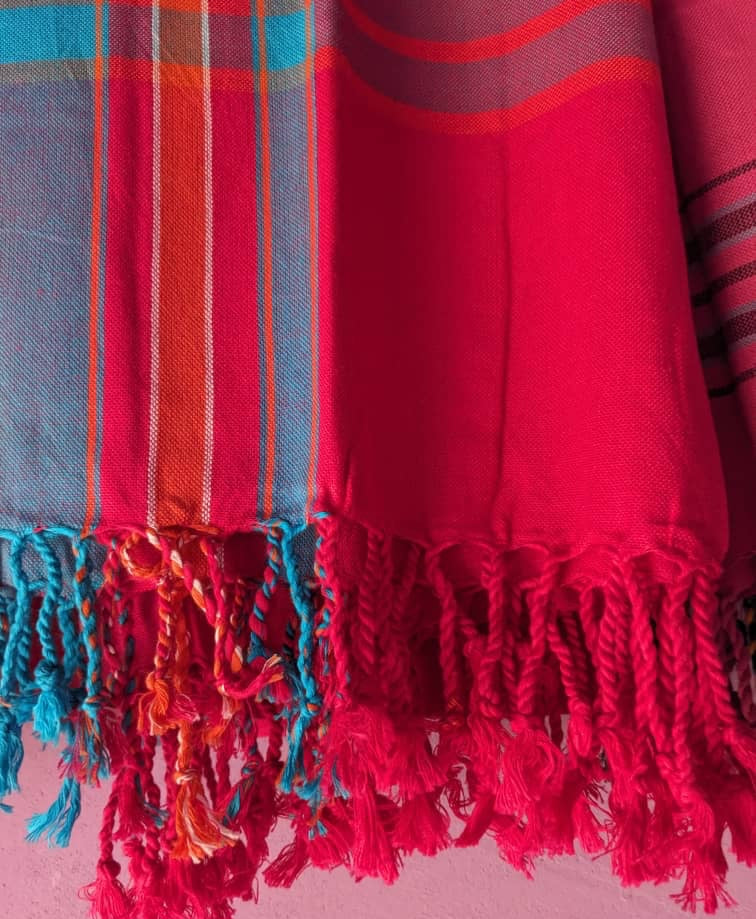 Red and turquoise throw rug with fringe on a pink background