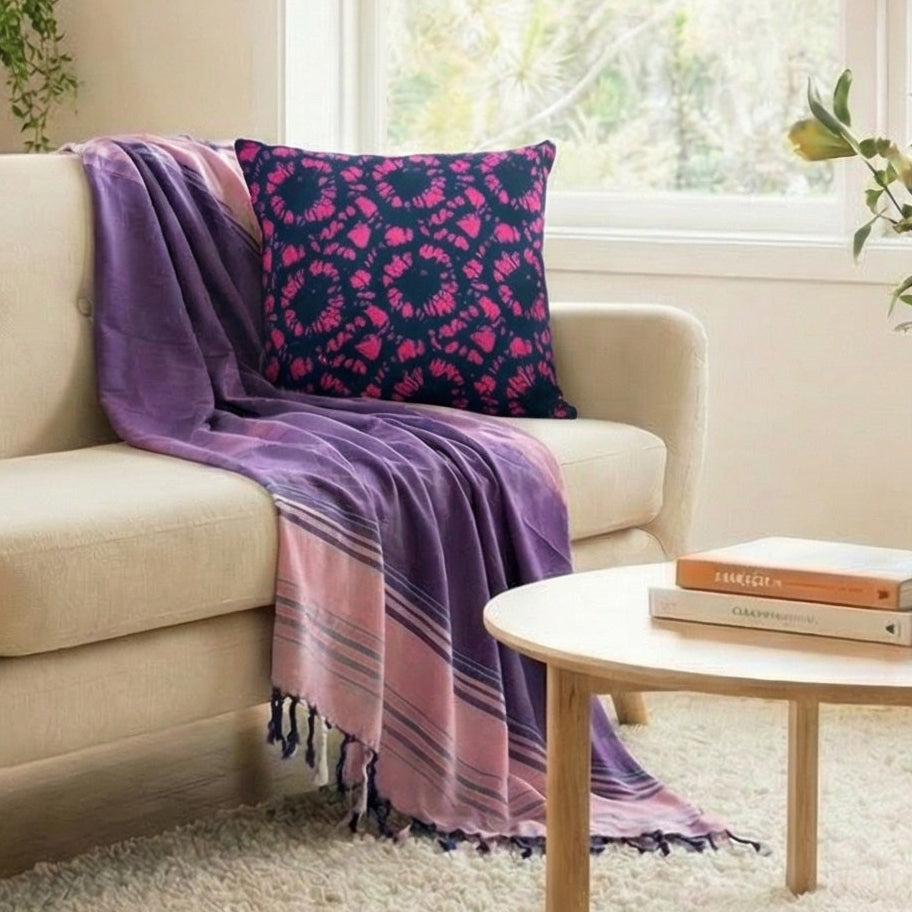 Living room with a beige sofa, purple blanket, and cushion, surrounded by plants.