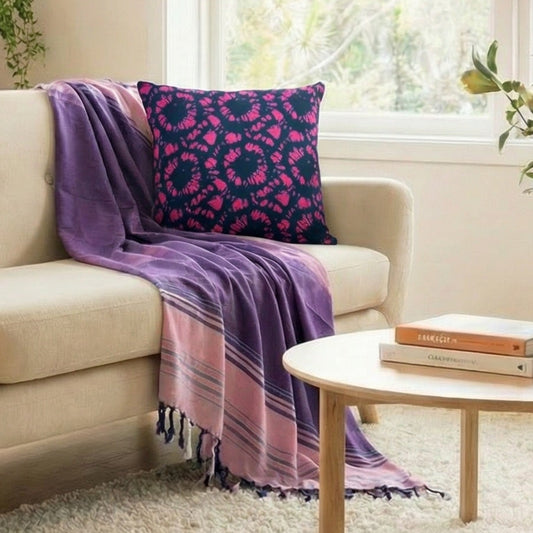 Living room with a beige sofa, purple blanket, and cushion, surrounded by plants.