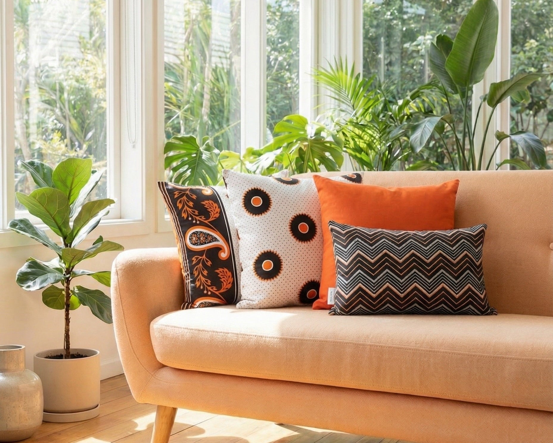 Light orange sofa with orange, black and white cushions in a sunlit room with large windows and plants.
