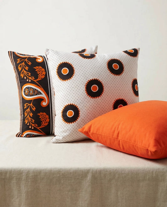 Three decorative cushions in orange, black and white on a neutral background