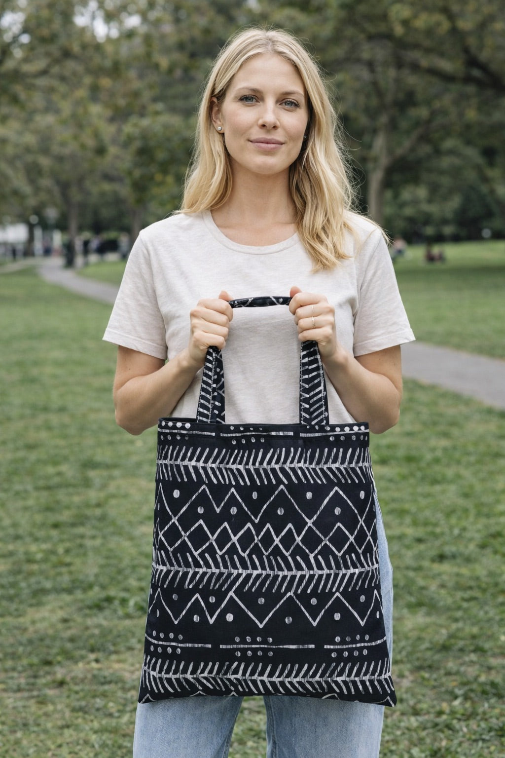 Woman holding a black and white patterned tote bag outdoors.